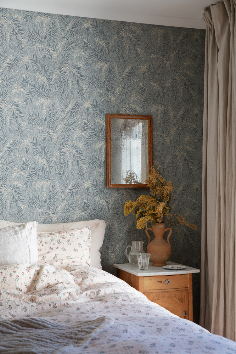 Idun, Nature Pattern Wallpaper in light blue featured on a wall of a bedroom with a bed with a patterned sheets and pillows.