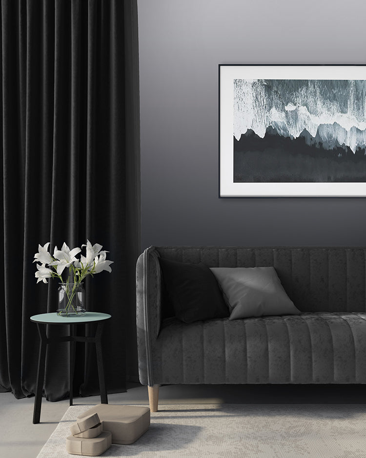 Modern room featuring Calbri Ombre Wallpaper, transitioning from grey at the base to a lighter hue at the top. Complemented by a dark grey velvet sofa, a green round table with white lilies, and abstract art.